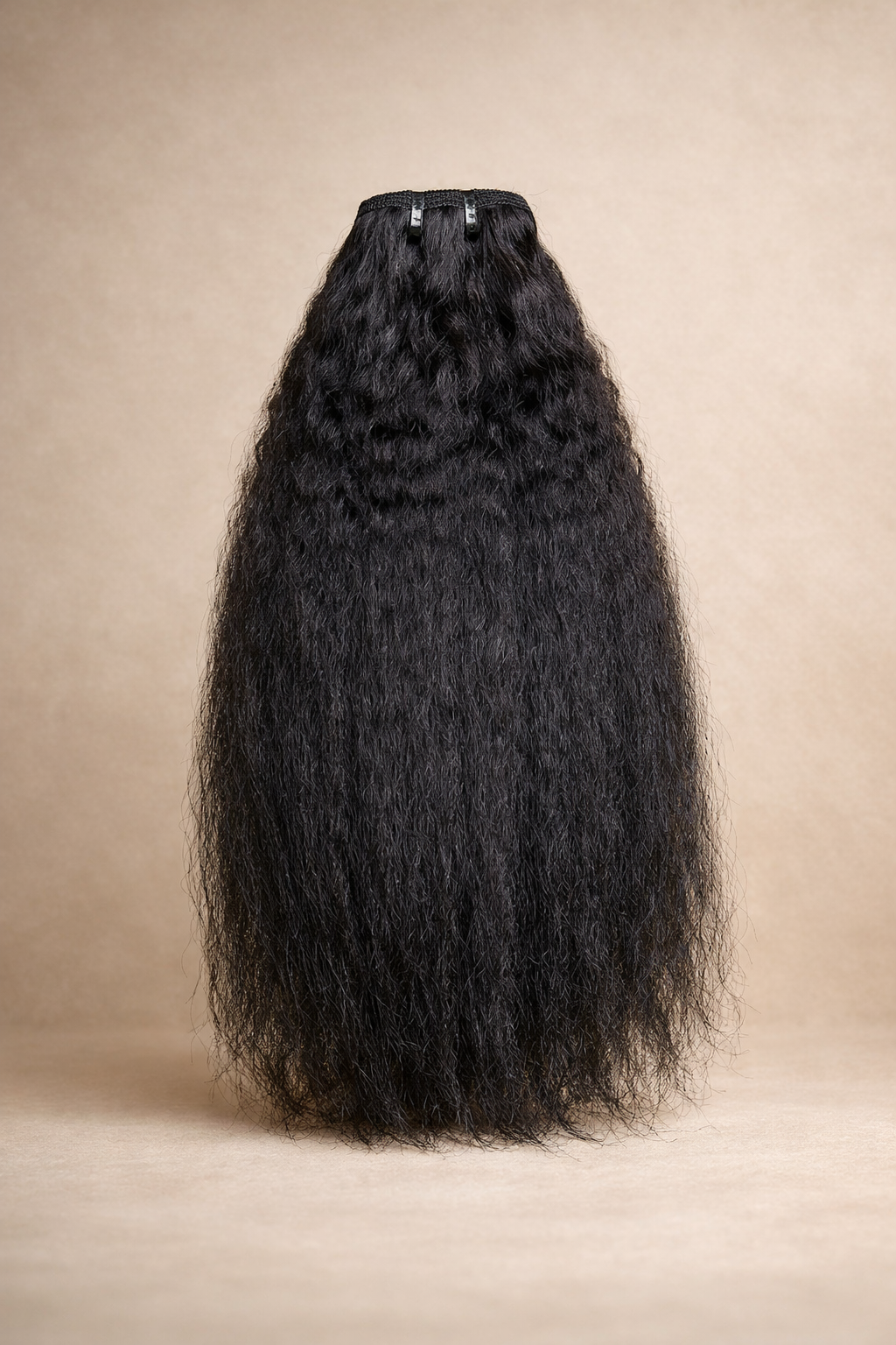 Long black curly hair extensions hanging against a beige background