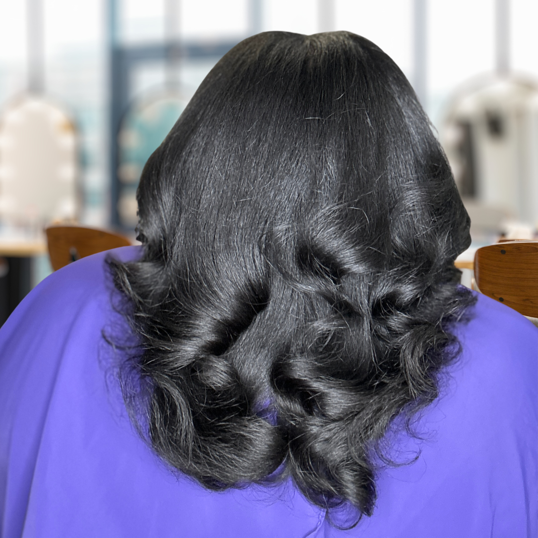 Back view of person with long black curly hair, wearing a purple top, seated indoors