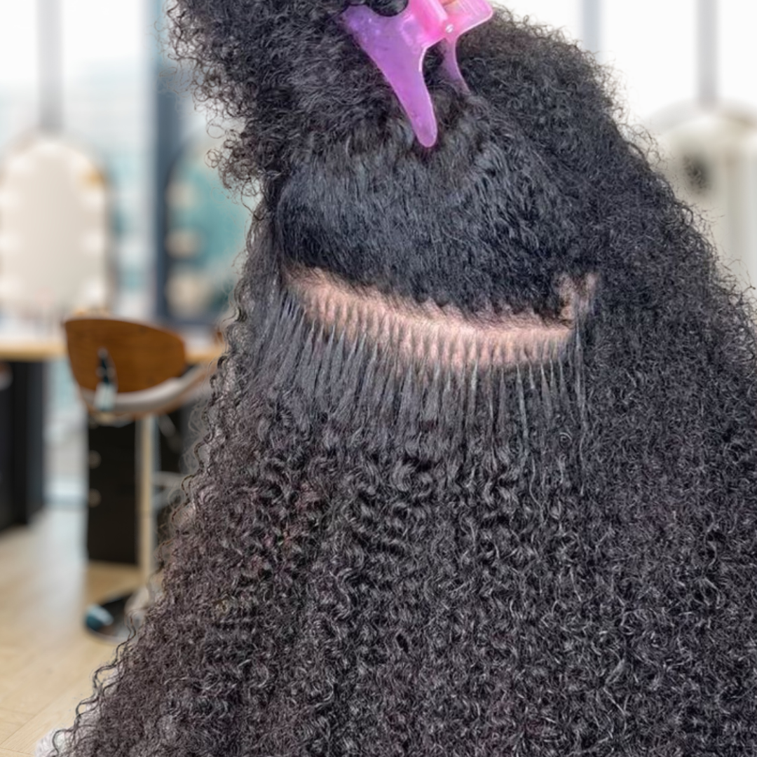 Close-up of curly black hair being sectioned with a pink clip, showing a neat horizontal part.