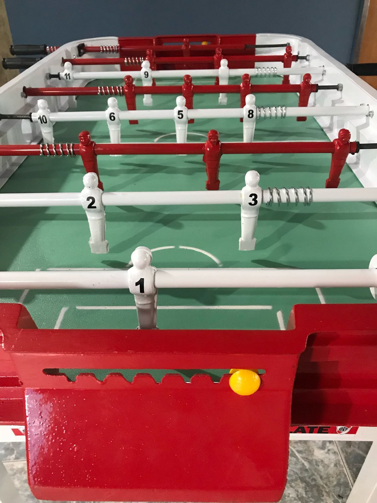 Una mesa de futbolín blanca y roja con una superficie de juego verde sobre un fondo blanco liso.