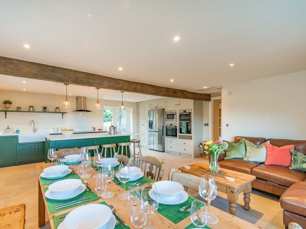 Open-plan kitchen/dining/living area. Dining table set for a meal, green kitchen island, brown leather sofa.