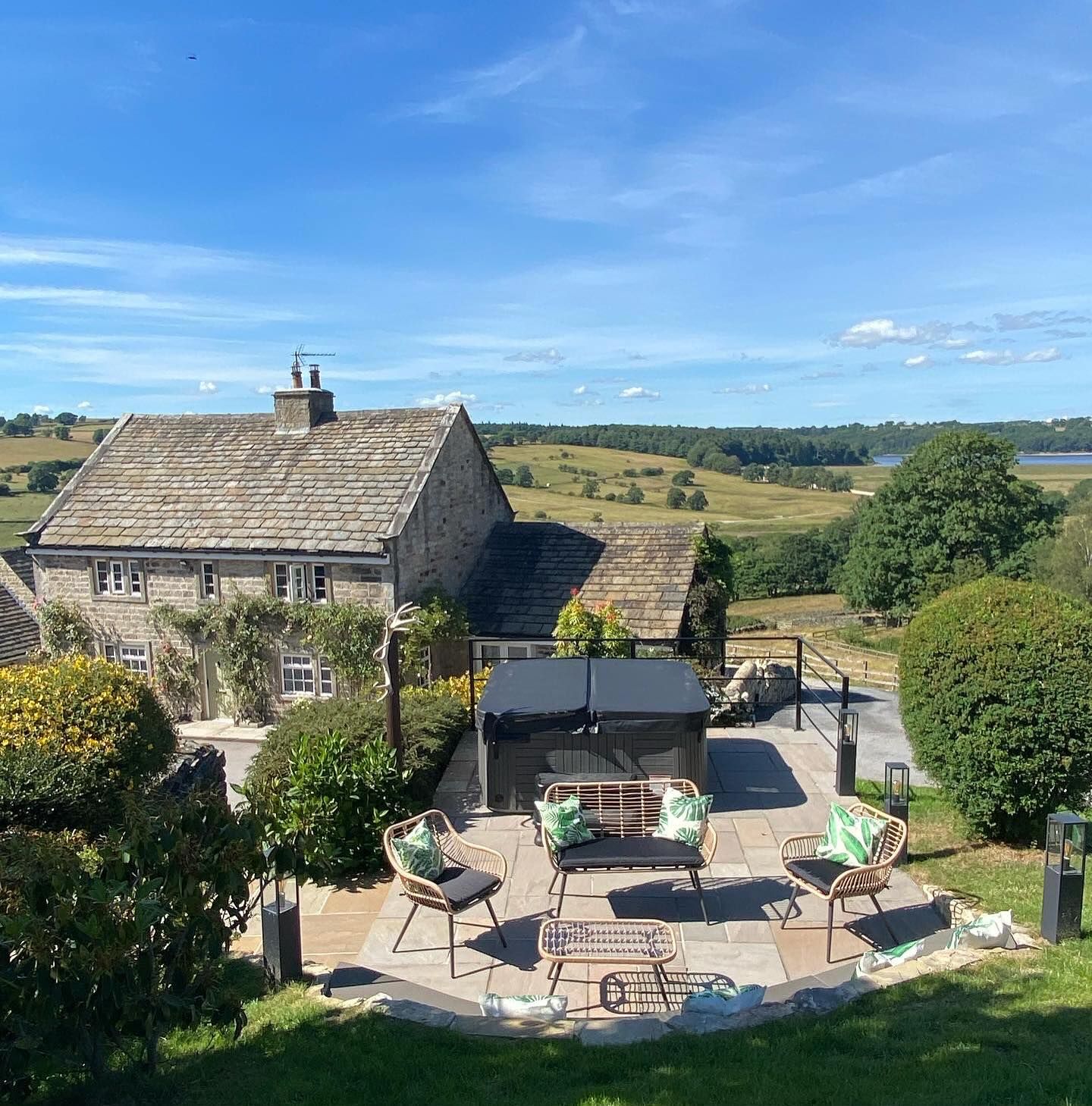 Stone house with patio, hot tub, seating, and expansive green landscape under a blue sky.