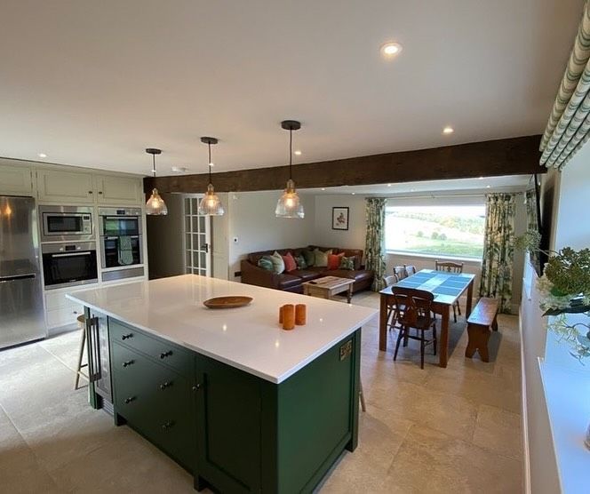 Spacious open-plan kitchen with green island, stainless steel appliances, and leather sofa in the living area.