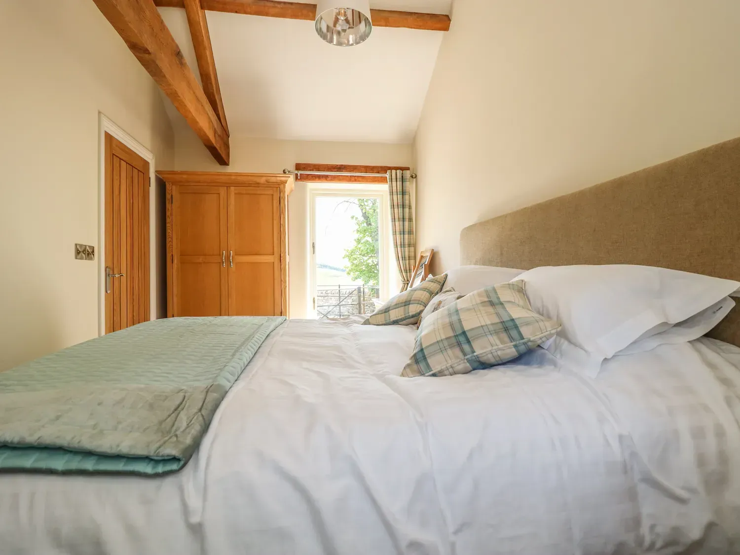 Bedroom with white bedding, teal blanket, wood beams, and an open door.