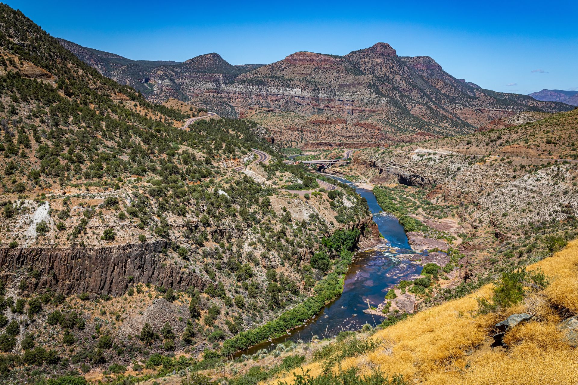 River cutting through a rugged canyon with mountains and sparse vegetation under a clear blue sky.