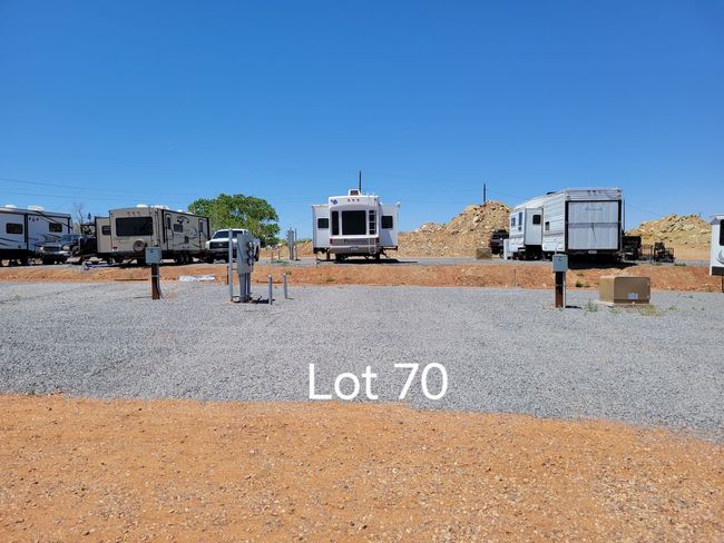 Large brown RV parked on gravel and concrete, with open door and awning, sunny outdoors.
