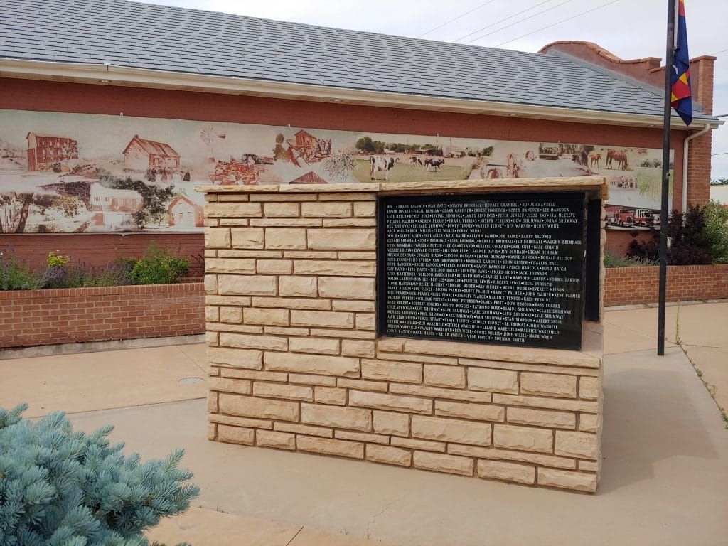 Stone memorial with a black plaque and a mural of a town in the background.