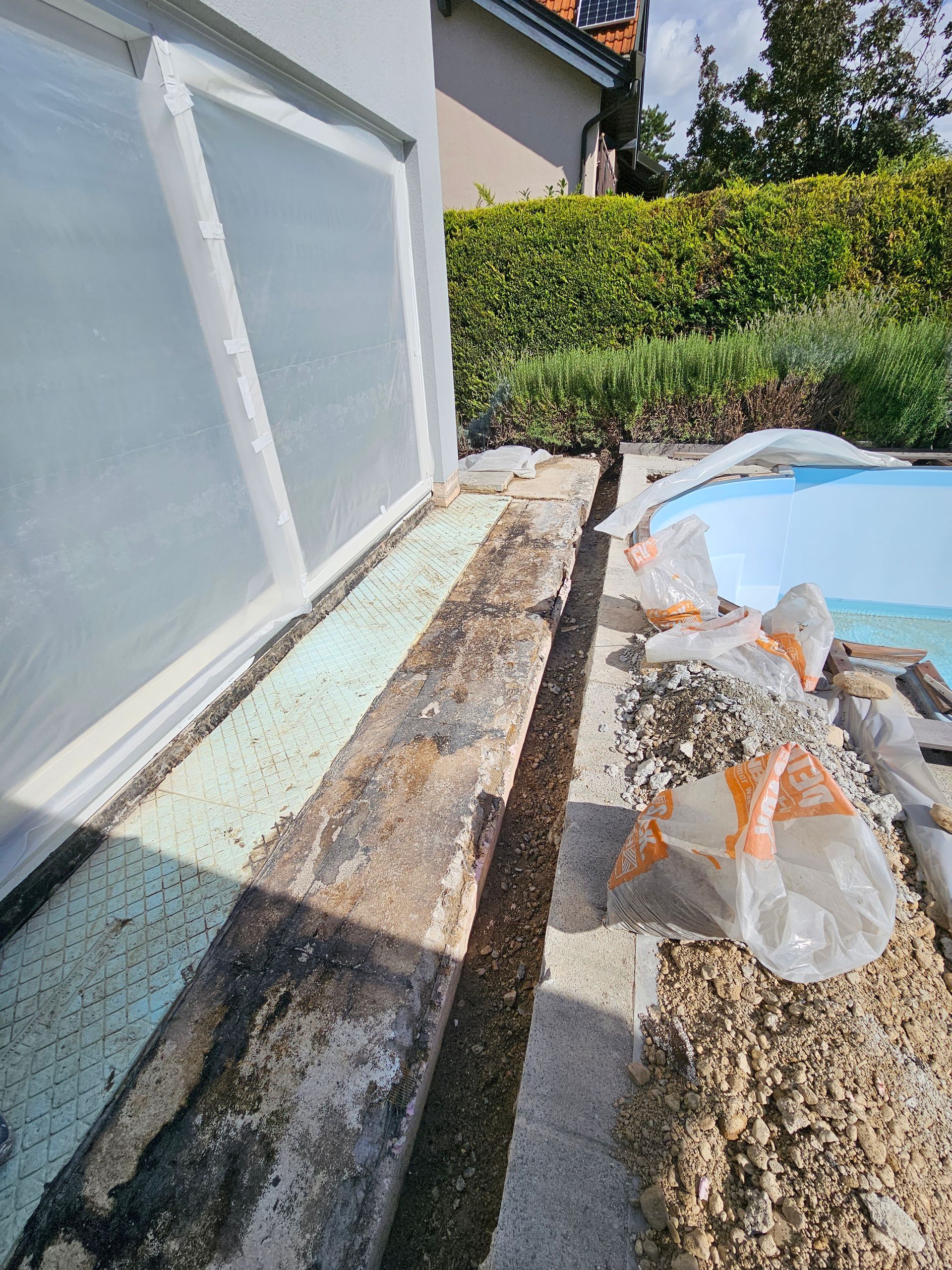 Bauarbeiten neben einem Haus und einem Swimmingpool, zu sehen sind ein Graben, Dämmplatten und verstreuter Bauschutt.