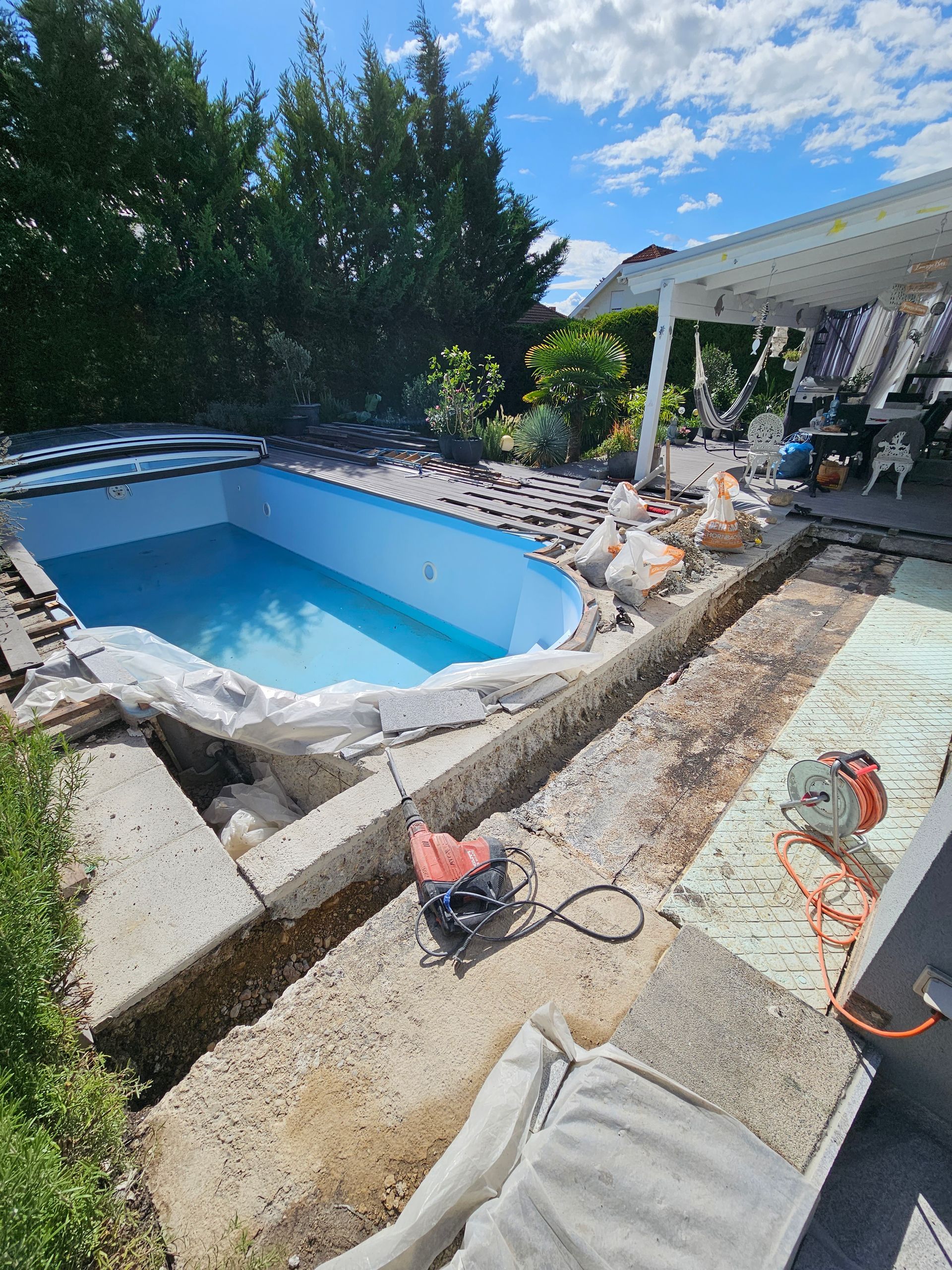 Ein im Umbau befindlicher Swimmingpool im Garten, mit freiliegenden Betonrändern, einem blauen Innenraum und Bauwerkzeugen.