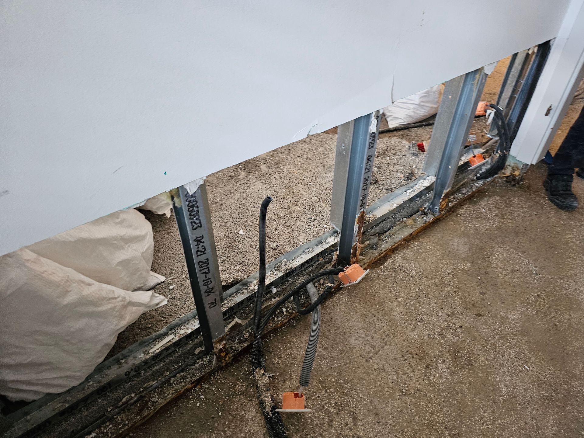 Eine im Bau befindliche Wand mit freiliegenden Metallständern, Kabeln und Elektroverteilerkästen in Bodennähe.
