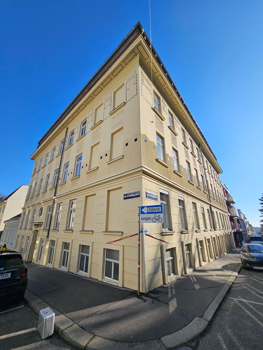 Ein hellgelbes, dreistöckiges Eckwohnhaus unter strahlend blauem Himmel in einer Stadtstraße.