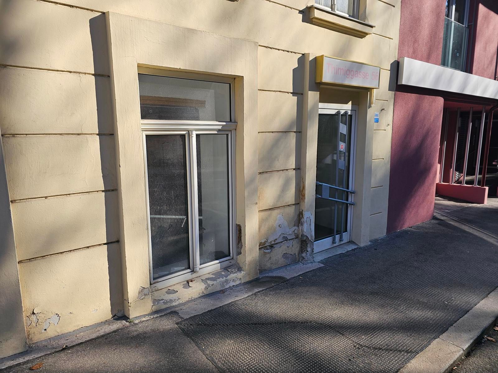 Ein beigefarbenes Ladenlokal mit großem Schaufenster und Glastür an einem Bürgersteig, dessen untere Wände Gebrauchsspuren aufweisen.
