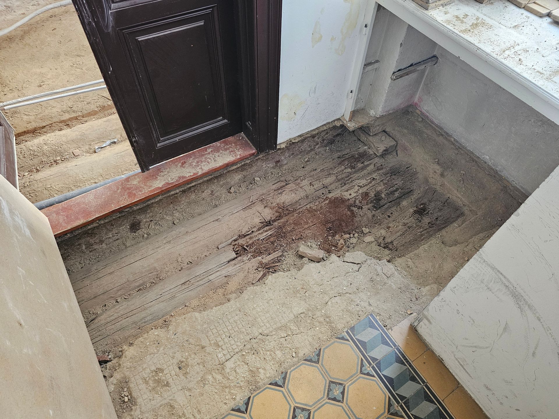 Ein Küchenboden mit freiliegendem, beschädigtem Beton und einem gemusterten Fliesenbereich in der Nähe einer Außentür.