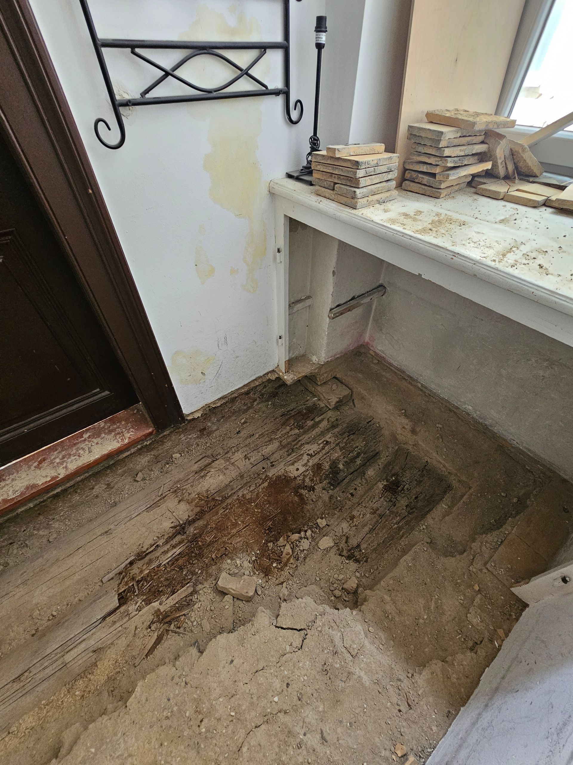 In einem Raum mit einem weißen Tisch und Holzbausteinen befinden sich eine beschädigte, fleckige Stelle am Fußboden und eine wassergeschädigte Wand.