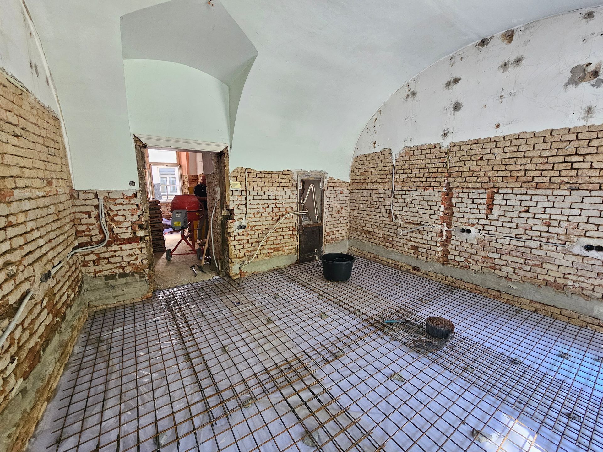 Renoviertes Zimmer mit freigelegten Ziegelwänden, Gewölbedecke und auf dem Boden verlegten Fußbodenheizungsrohren.