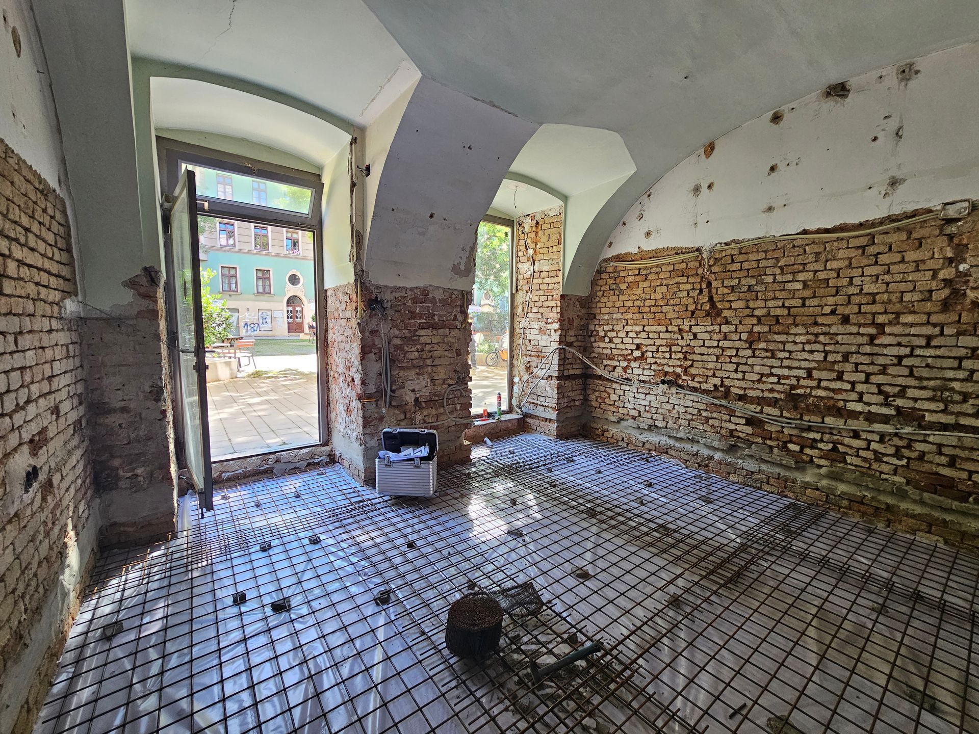 Ein Innenraum im Umbau mit freiliegenden Ziegelwänden, gewölbter Decke und einem Raster für eine Fußbodenheizung.