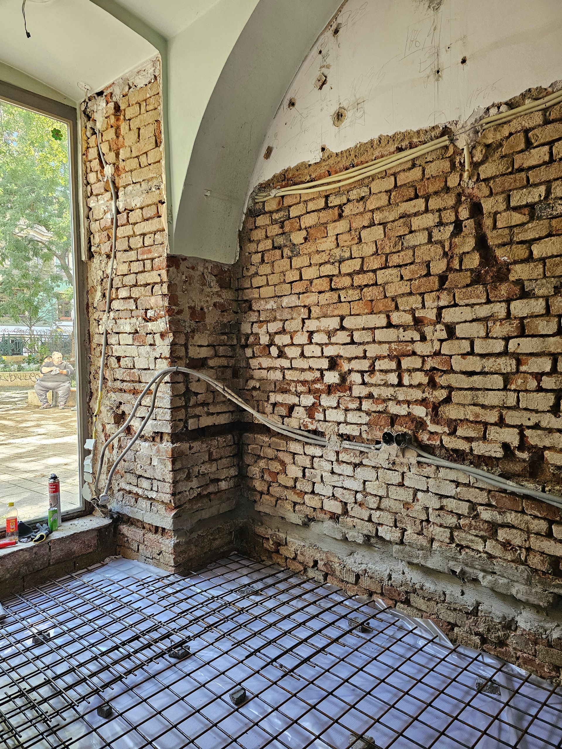 Ein Raum, der gerade renoviert wird und über freiliegende Ziegelwände, eine gewölbte Decke und einen Metallgitterboden auf einer Unterlage verfügt.