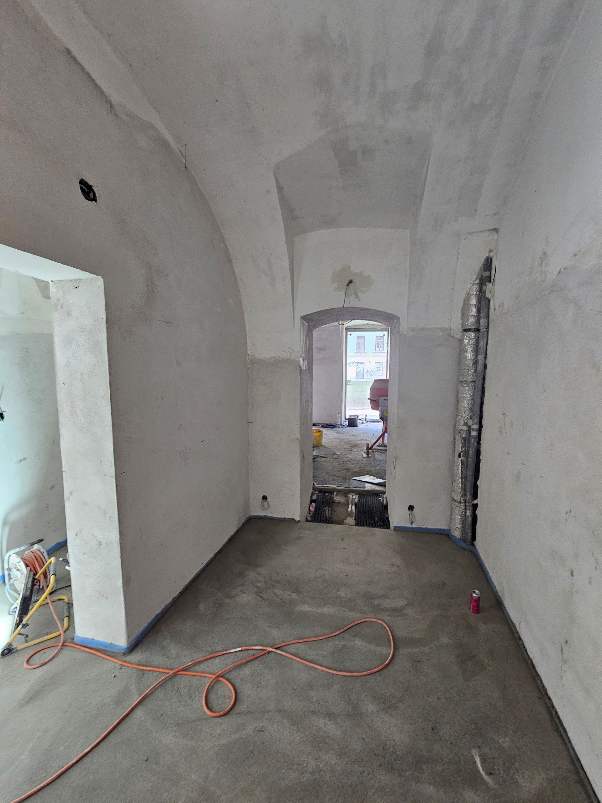 Innenansicht eines im Bau befindlichen Raumes mit gewölbten Decken, unverputzten Wänden und einem orangefarbenen Stromkabel.