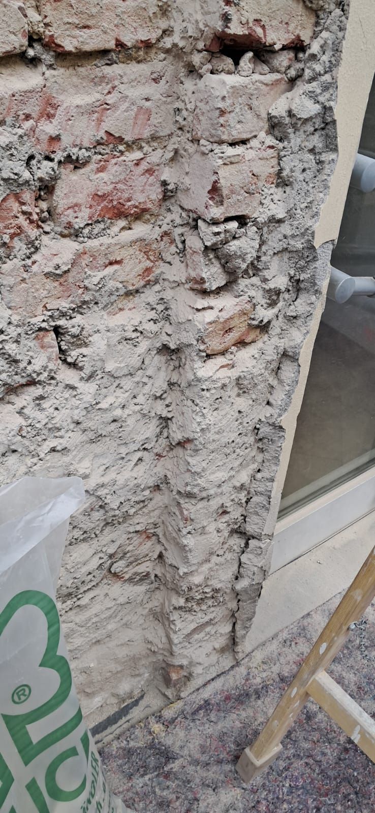 Nahaufnahme einer beschädigten Ziegelmauer mit freiliegendem Mörtel und unebenem Putz, die renoviert wird.