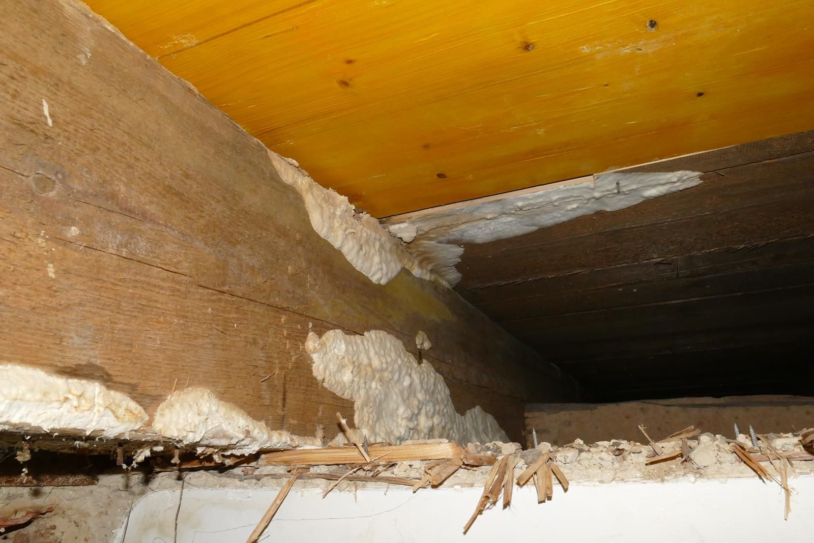 In einem Kriechkeller wurde Dichtungsschaum zur Abdichtung der Spalten zwischen einem rauen Holzbalken und einer hölzernen Deckenplatte verwendet.