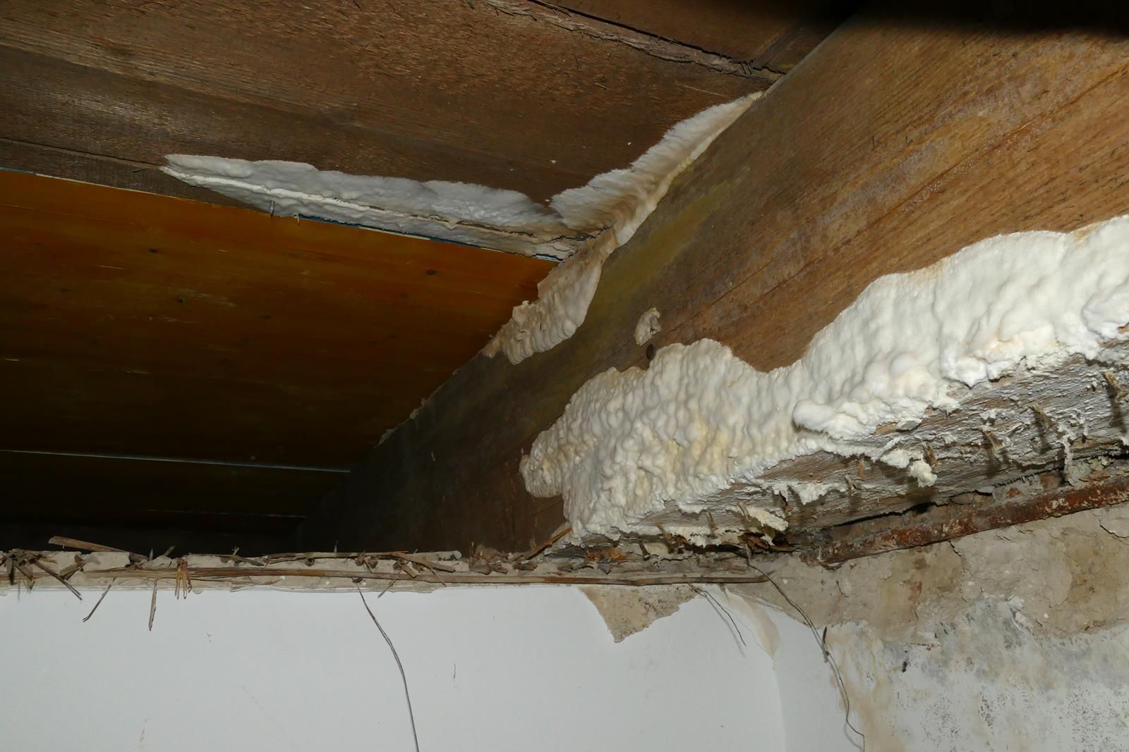 Auf einen Holzbalken über einer Gipskartondecke aufgetragener Expansionsschaum-Dichtstoff.