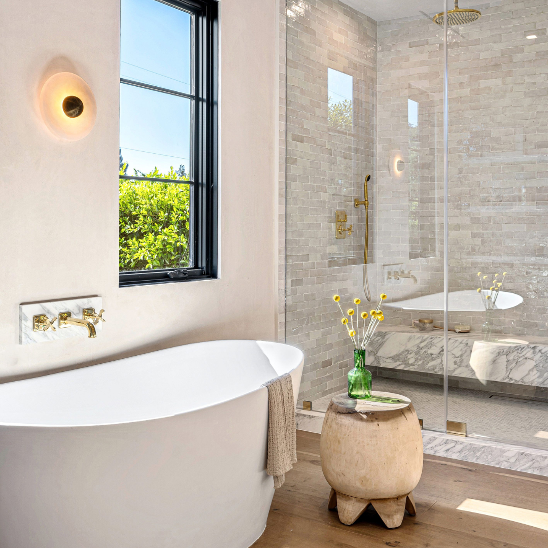 Modern bathroom with freestanding tub, glass shower, black window, and small round stool with flowers