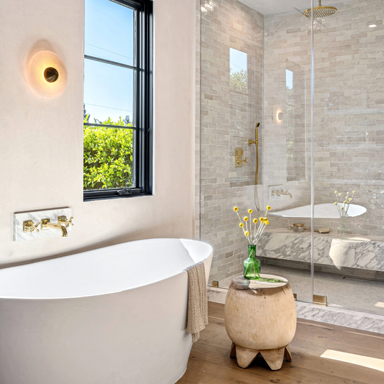Modern bathroom with freestanding tub, glass shower, window, and small stool with flowers