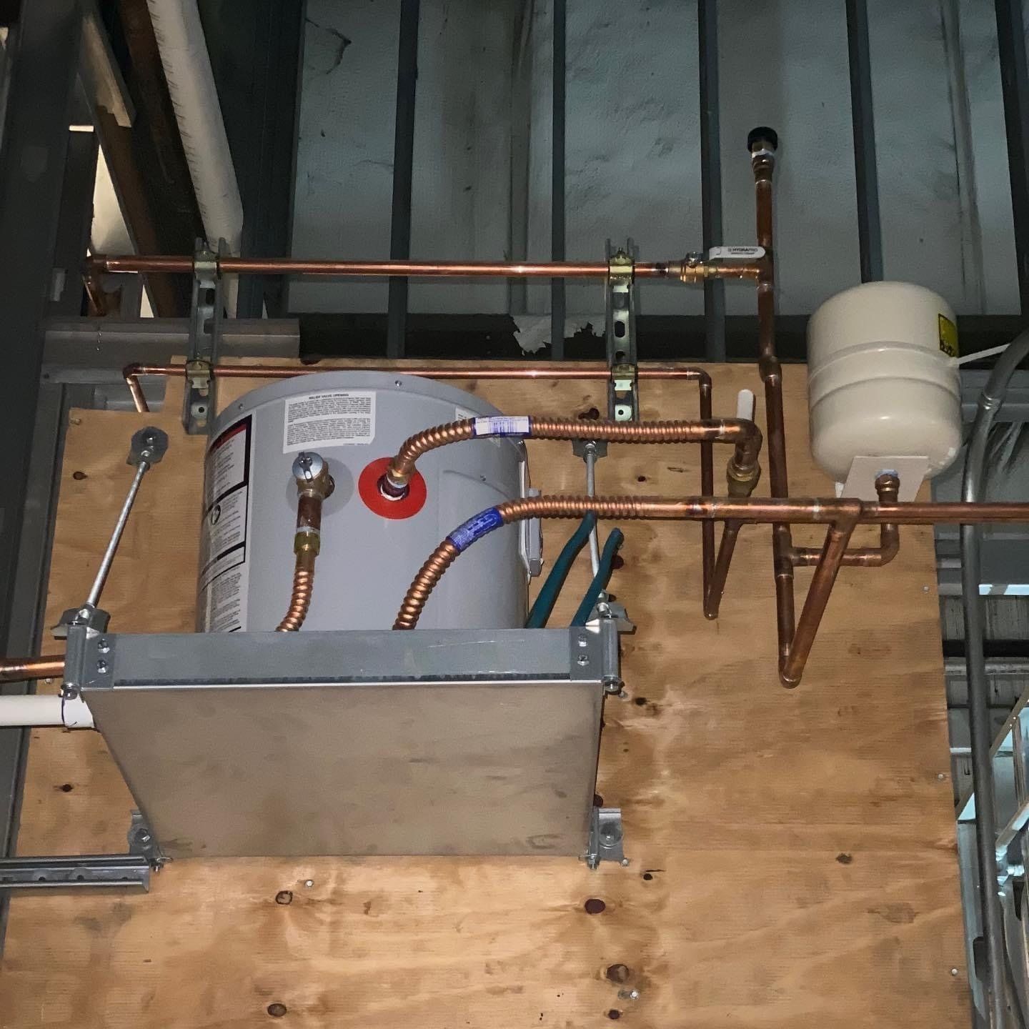 Industrial utility equipment with copper pipes, hoses, and a metal tank mounted against plywood and wall framing