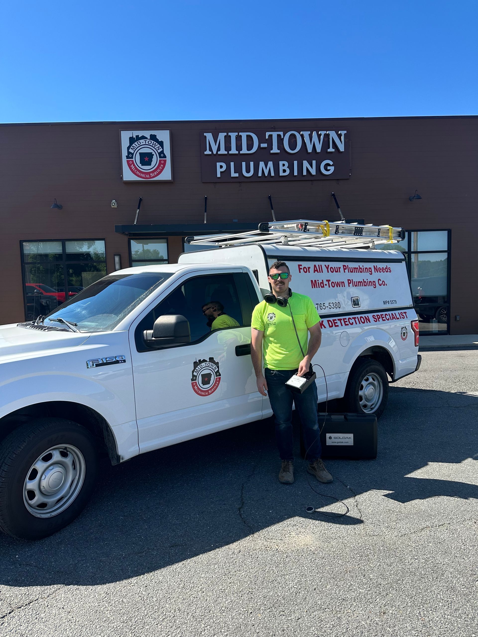 Mid-Town Plumbing worker beside white service van in front of storefront sign