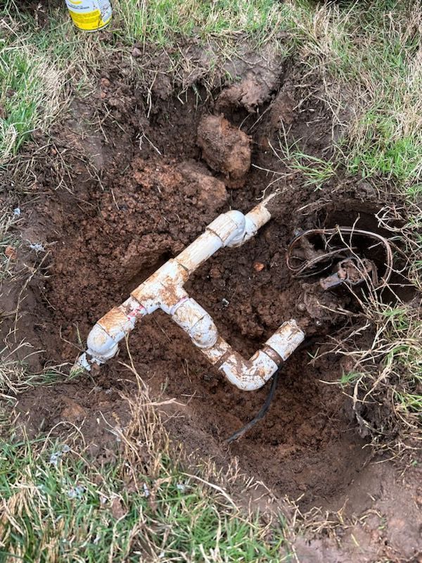 Excavated soil around a buried white PVC pipe fitting in a grassy yard