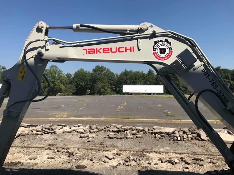 Takeuchi excavator arm over a dirt construction site under a clear blue sky