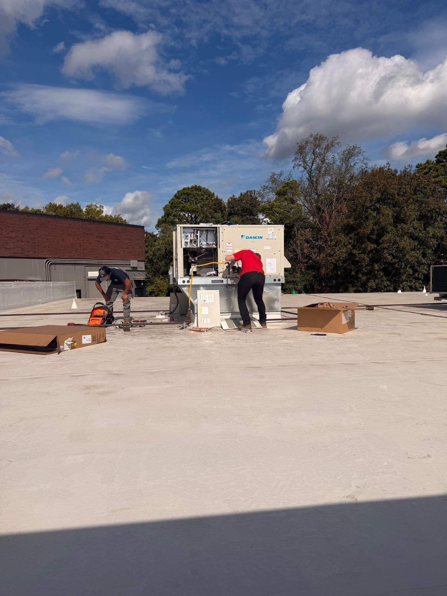 Workers on a rooftop installing equipment under a blue sky, with tools and materials scattered nearby.