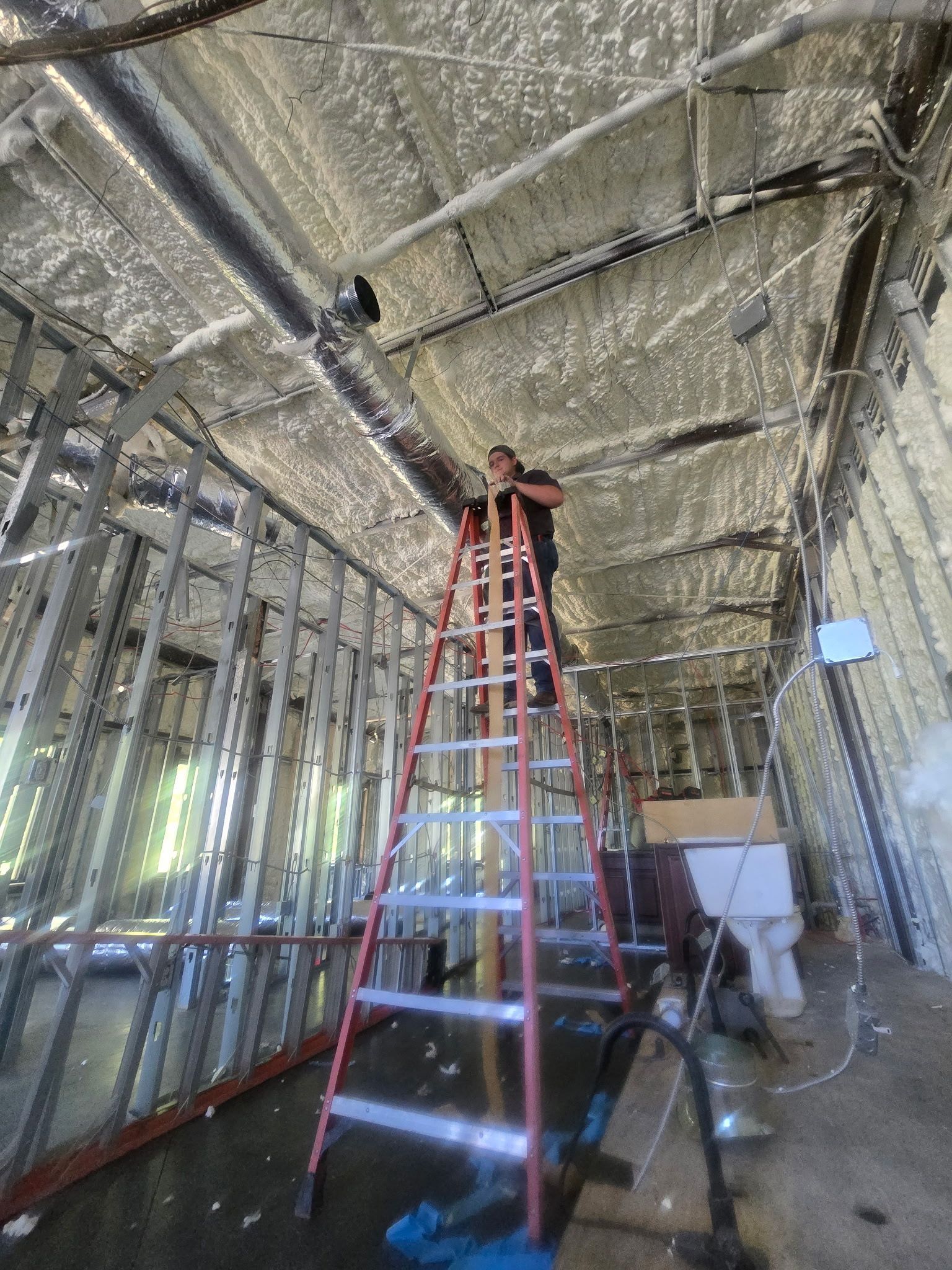 Worker on a red ladder installing reflective insulation in a framed room under construction.