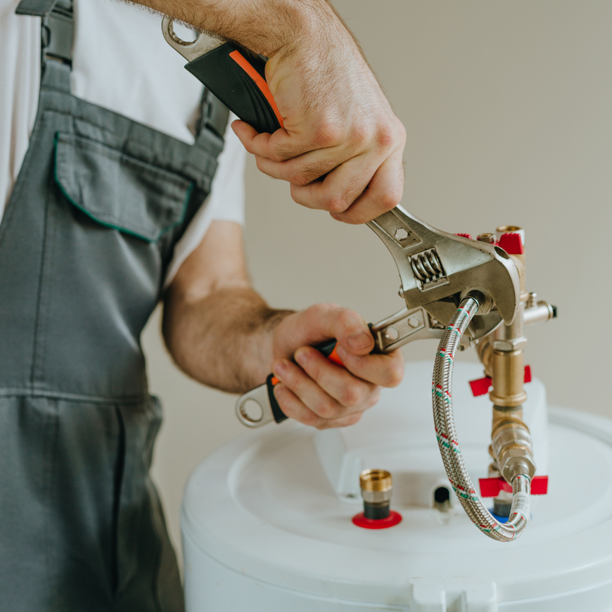 Hands using a metal tool to connect a hose and fitting on a white tank or appliance.