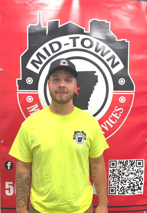 Man standing in a neon yellow shirt before a red Mid-Town Services banner with logo and QR code