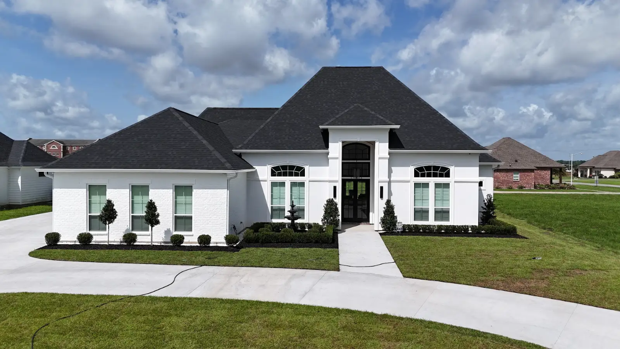 White modern single-story house with black roof and curved driveway on a green lawn under a partly cloudy sky