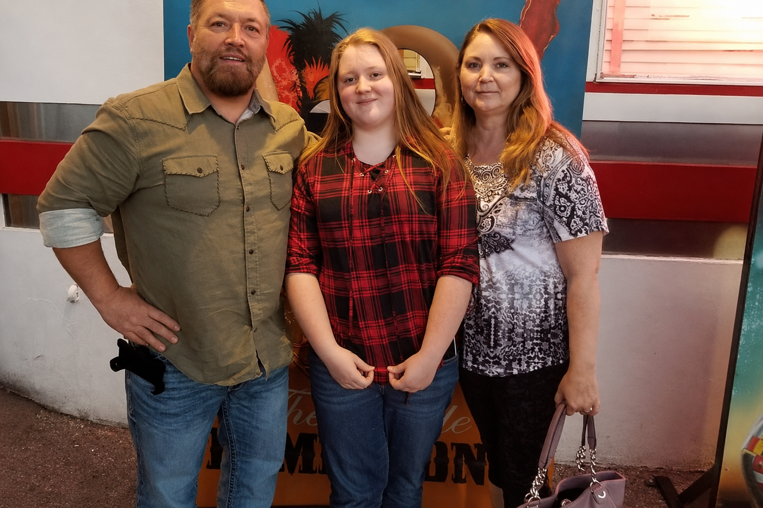 A family of three poses in front of a candy corn backdrop. A woman and man flank a baby held by the man.