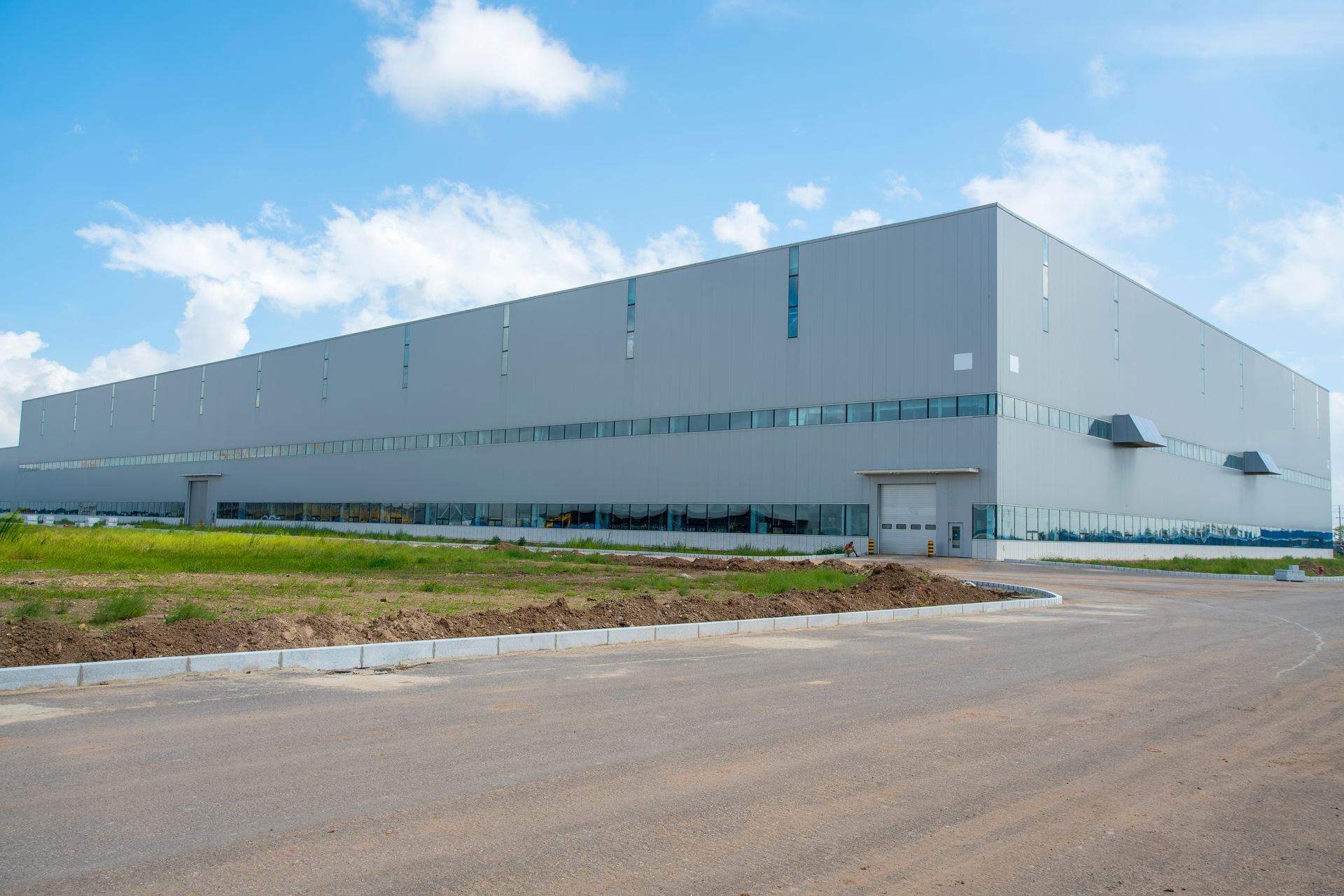 Large white industrial warehouse beside a paved road under a bright blue sky