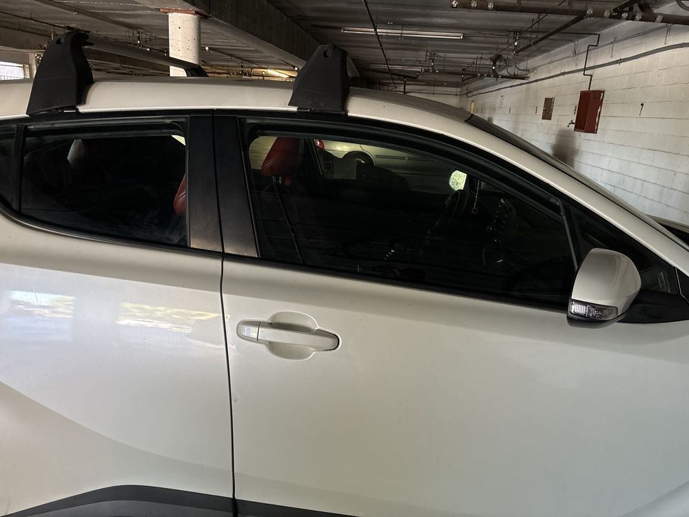 A white car with a roof rack is parked in a garage.