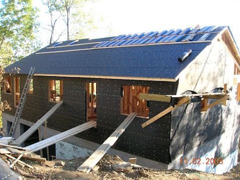 Partially built house with dark siding and roof, supported by wooden braces at a construction site