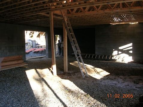 Partially framed room with ladder, sunlight streaming through openings, and construction materials inside.