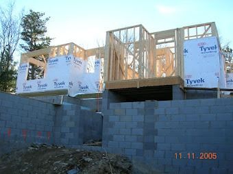 Partially built wooden house on cinder block foundation, wrapped in Tyvek, with clear sky above.