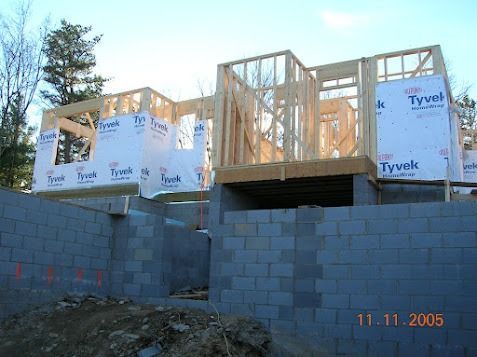 Partially built house framing and Tyvek-wrapped walls on a cinder block foundation at a construction site