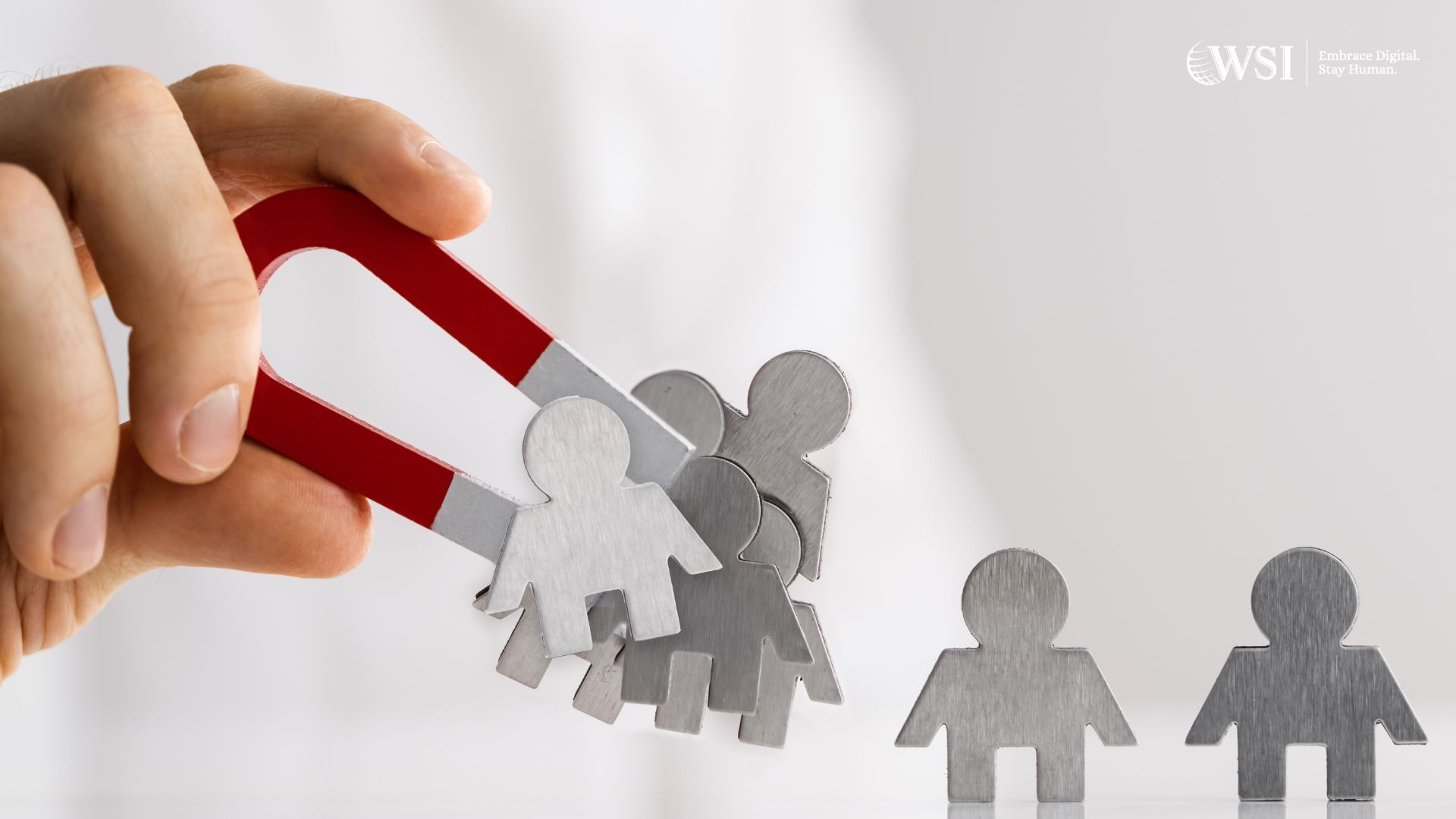 Hand holding a red and silver magnet attracting paper cut-out figures, with more figures nearby.