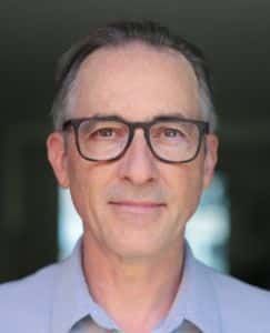 Seamus Smyth wearing glasses and a blue shirt is smiling for the camera .