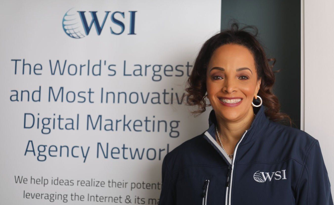 Kelly Biggs stands in front of a sign that says wsi