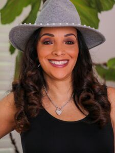 Kelly Biggs wearing a hat and a necklace is smiling.