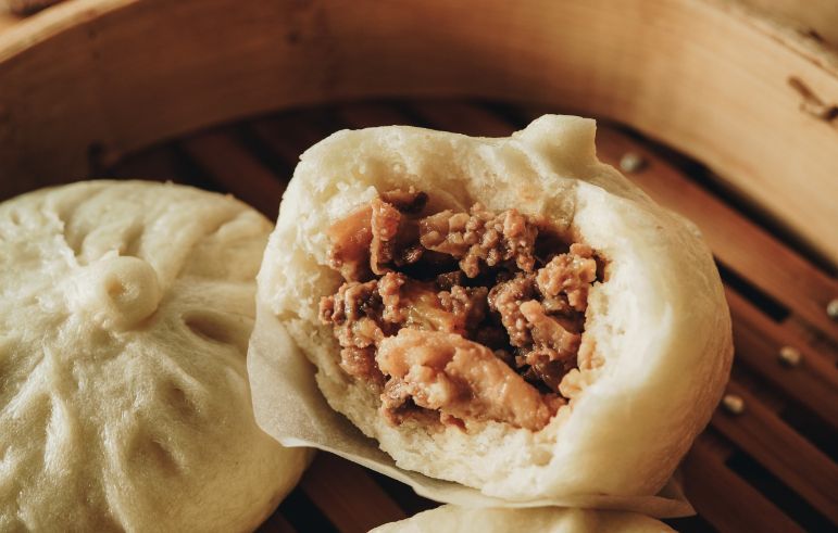 A close up of a dumpling with meat in it in a bamboo steamer.