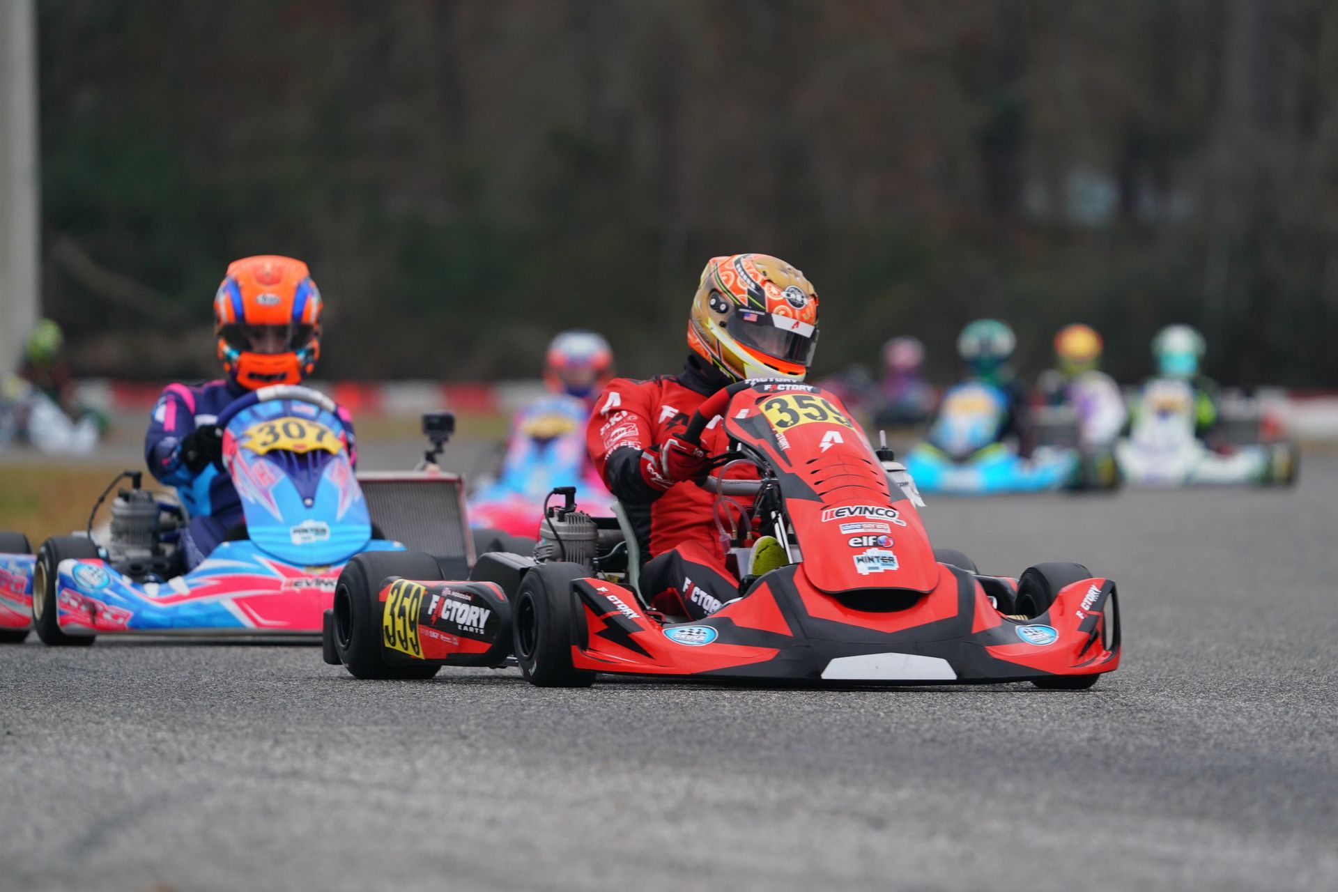 Go-kart racers speeding around a track, with a red kart leading a blue kart in the foreground