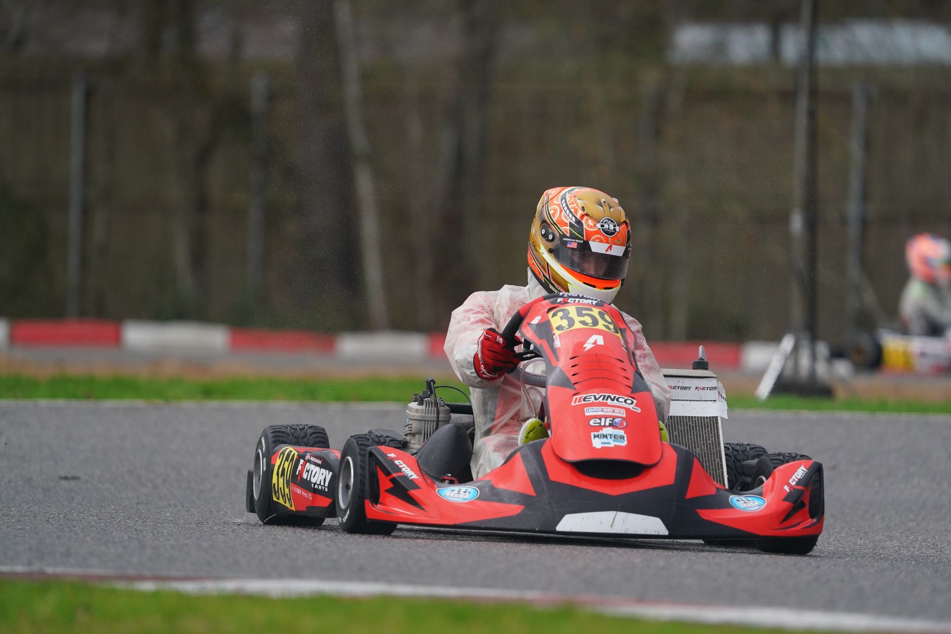Red go-kart racing on a wet track, driver in a red helmet steering through a curve.
